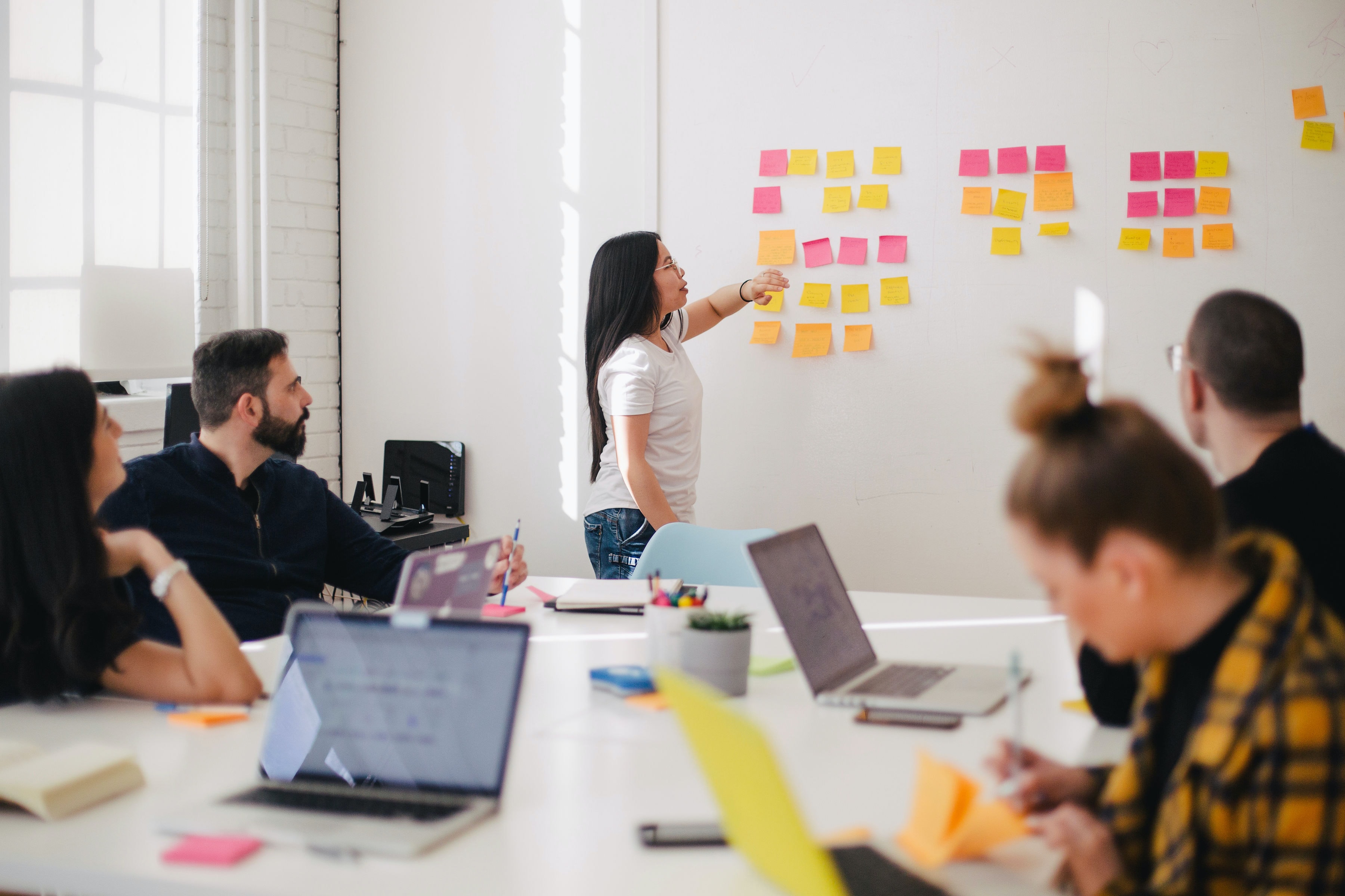 A woman facilitates a session using post-it notes and a whiteboard in front of a group of people