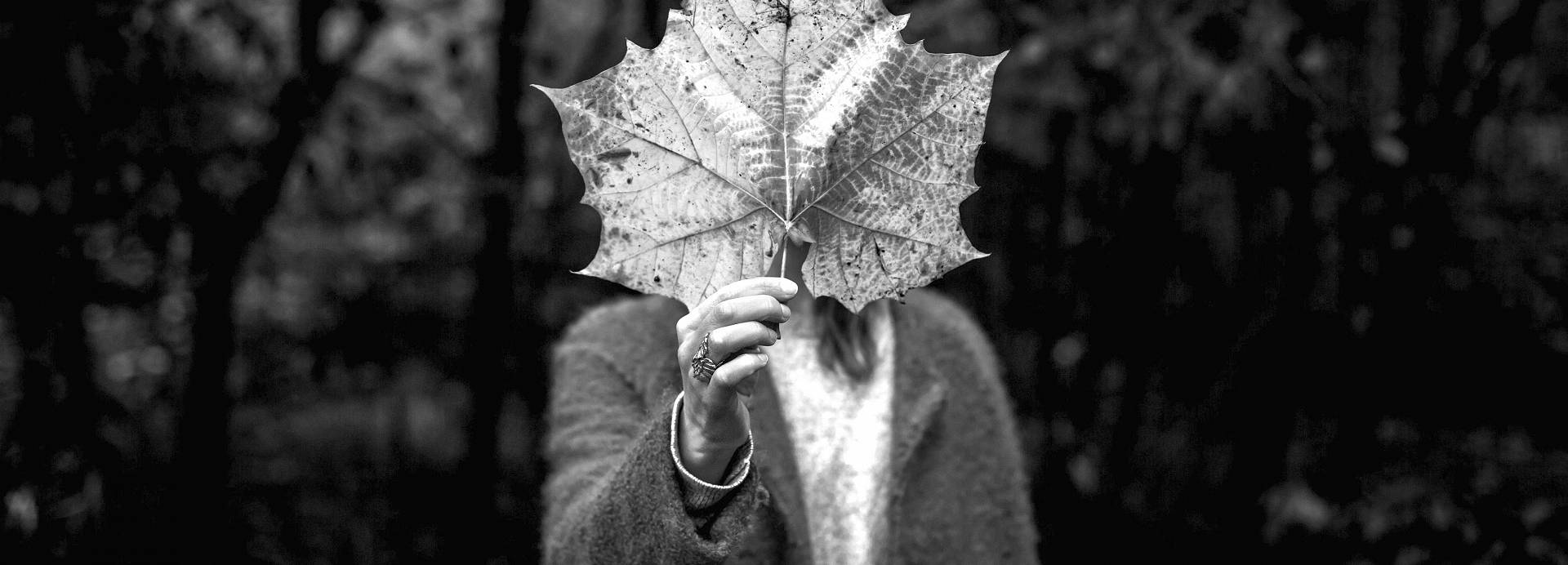 Woman holding a large five pointed leaf in front of her so that it covers her face