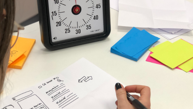 A young women takes part in a Active Eights activity at her desk, where there are also post-it notes and a timer.