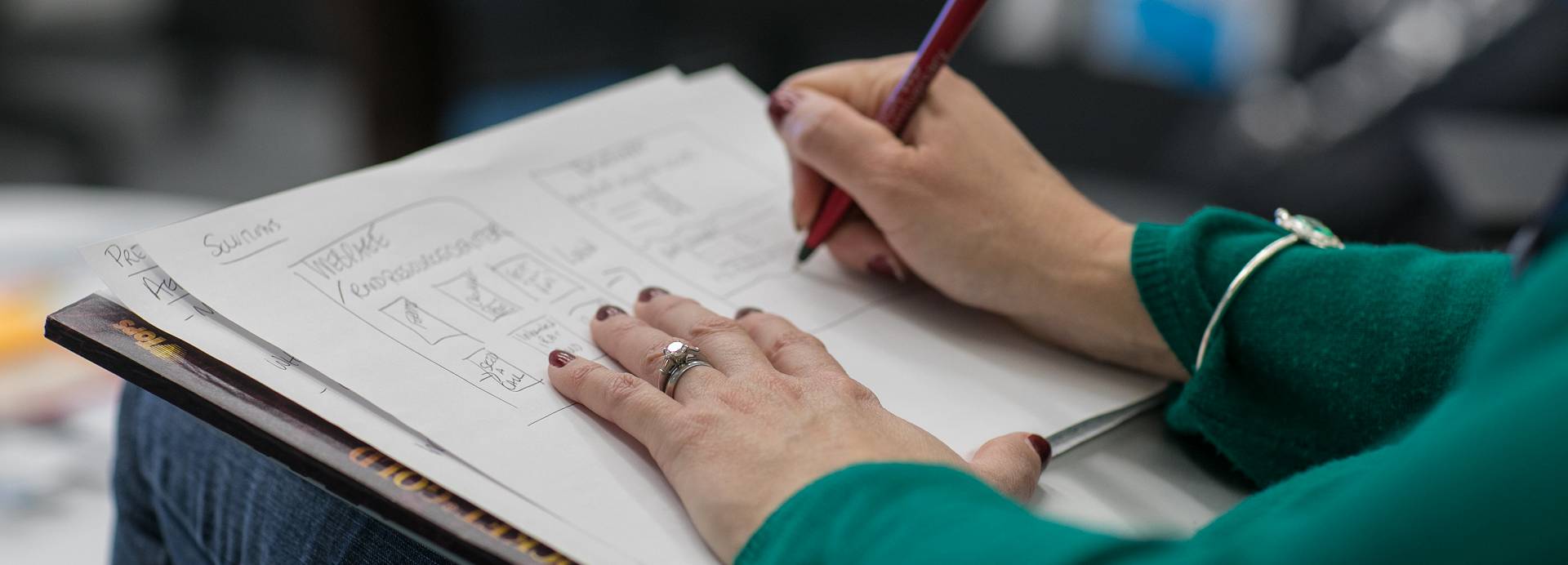 A person in a green jumper sketches out ideas on an A3 piece of paper.