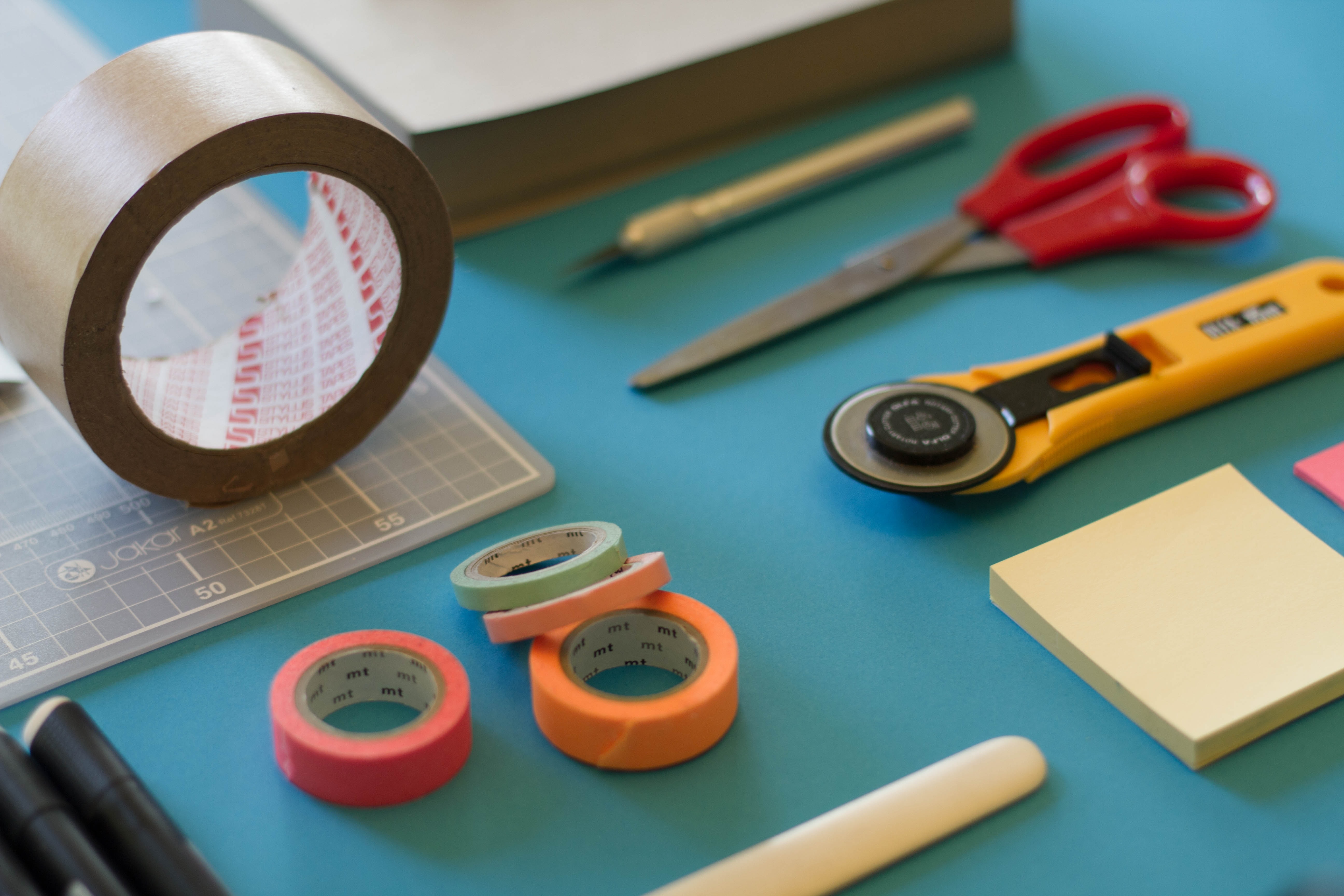 An array of stationery and craft items, including cutting tools, adhesives and tape, and sticky notes.