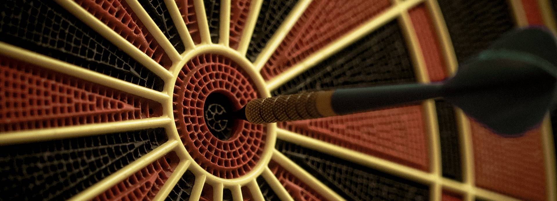 A black dart sticks out of the centre bullseye of a dartboard. Cropped to just show the middle third of the board.