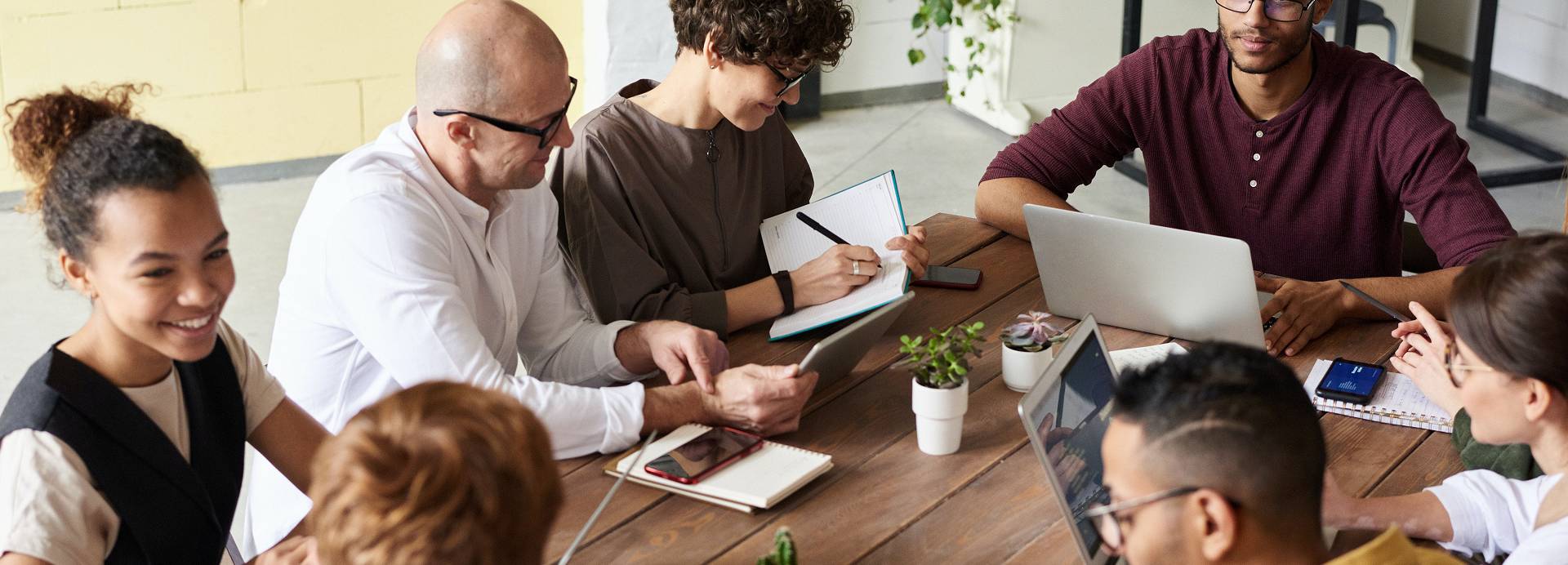 A group of people work together around a desk with a laptop and a tablet.
