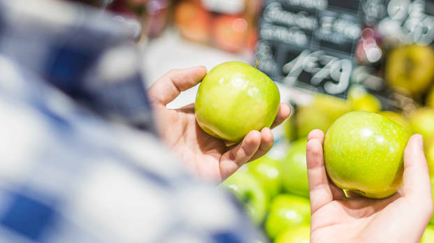 Man holding two green apples and trying to choose between them